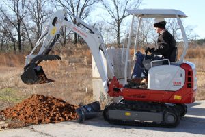 A man operating a TB216 Excavator on a job site. He is scooping dirt.