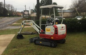 A tb216 excavator on a patch of grass with a sidewalk going down the left side