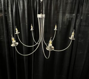 a 6 arm silver candle chandelier in front of a black drape