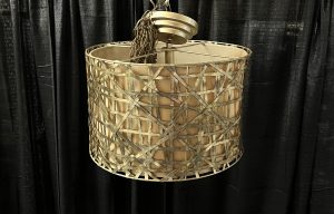 a gold circular chandelier wiht a basket weave design. the chandelier sits in front of a black drape.