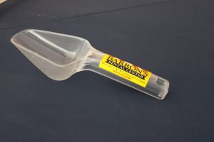 an opaque ice scoop with a yellow barrons rental center sticker on the handle. it sits on a black background