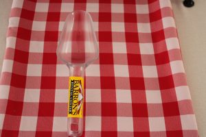 an opaque ice scoop with a yellow barrons rental center sticker on the handle. the scoop sits on a red and white checkered tablecloth.
