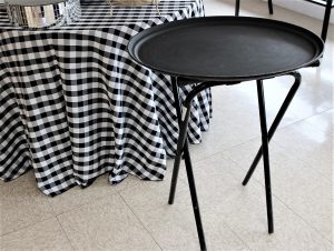 a black server tray sitting on a black stand. it sits next to a table with a black and white checkered table cloth